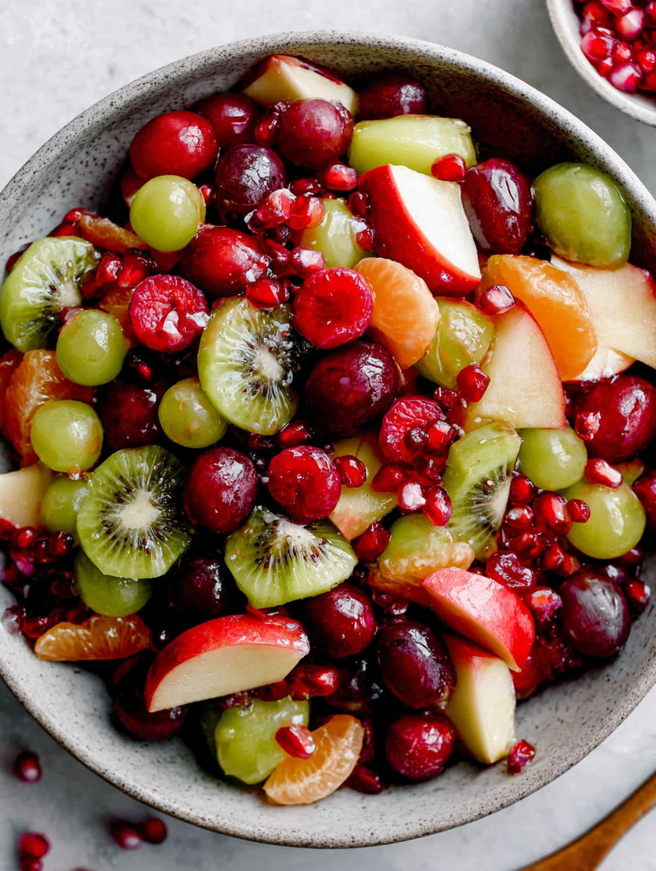 A bowl of fruit salad with kiwi, apples, oranges, and pomegranates.