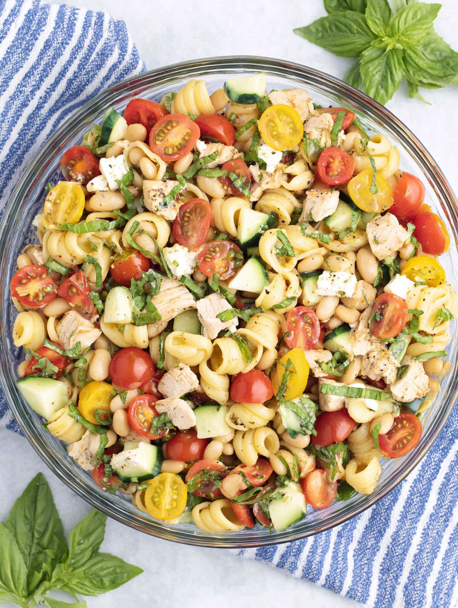 A bowl of pasta salad with tomatoes, cucumbers, beans, and chicken.