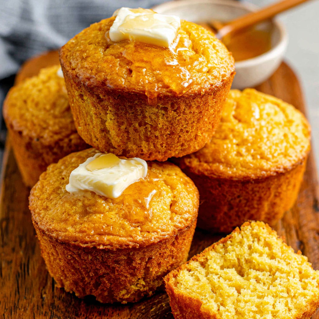 Three stacked cornbread muffins with butter on top.