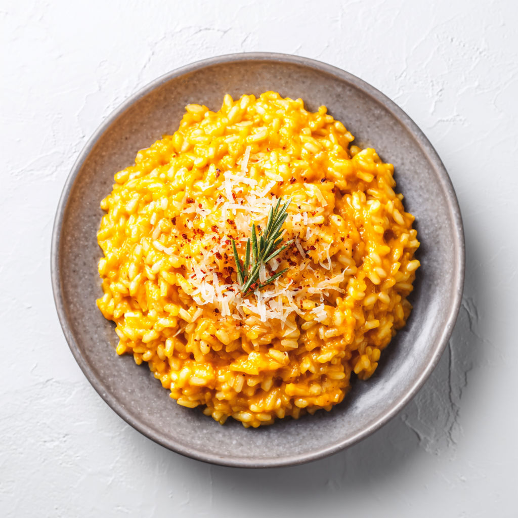 A bowl of creamy pumpkin risotto with cheese on top.