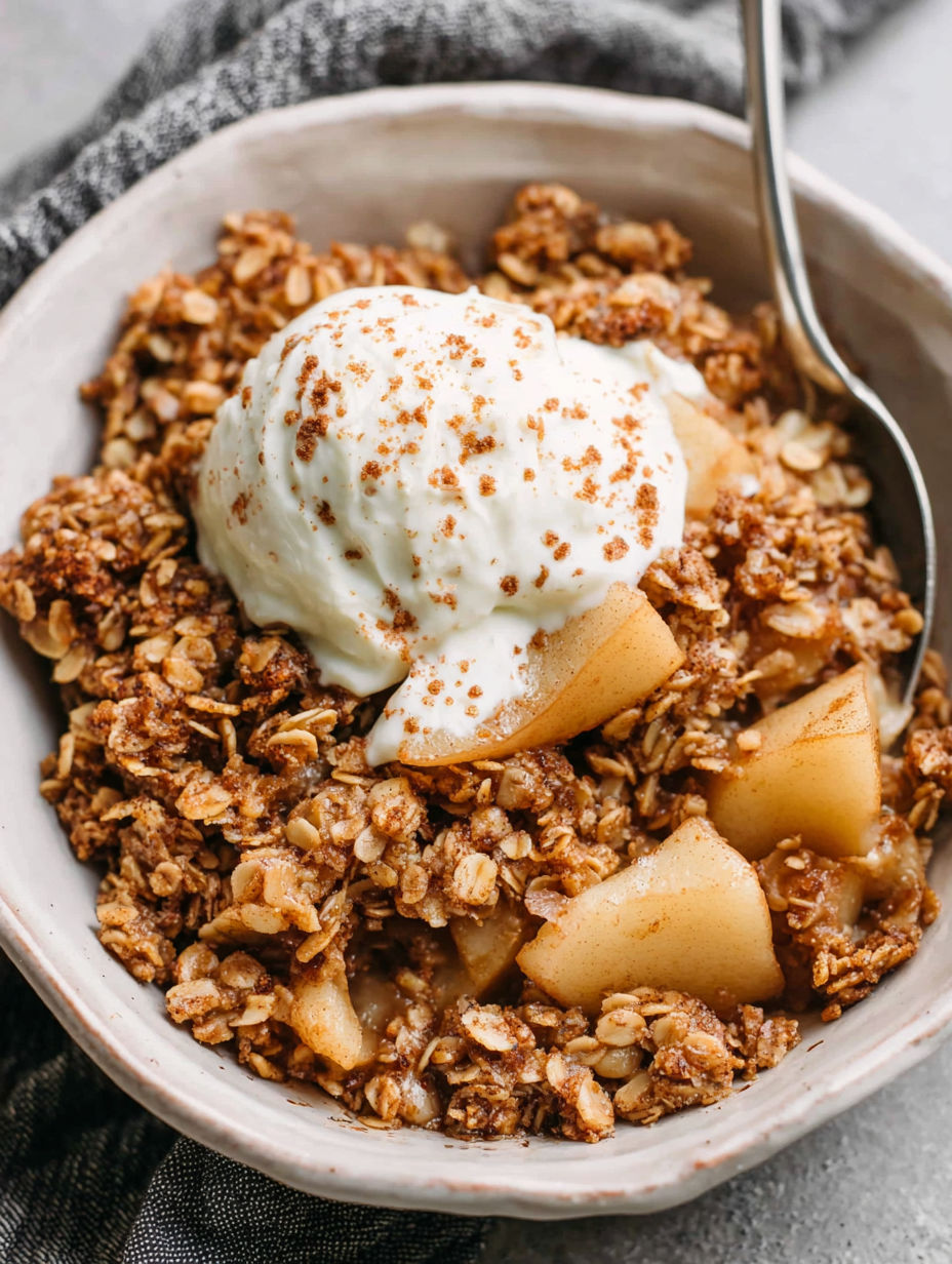 A bowl of cinnamon-spiced pear crisp with a dollop of whipped cream on top.