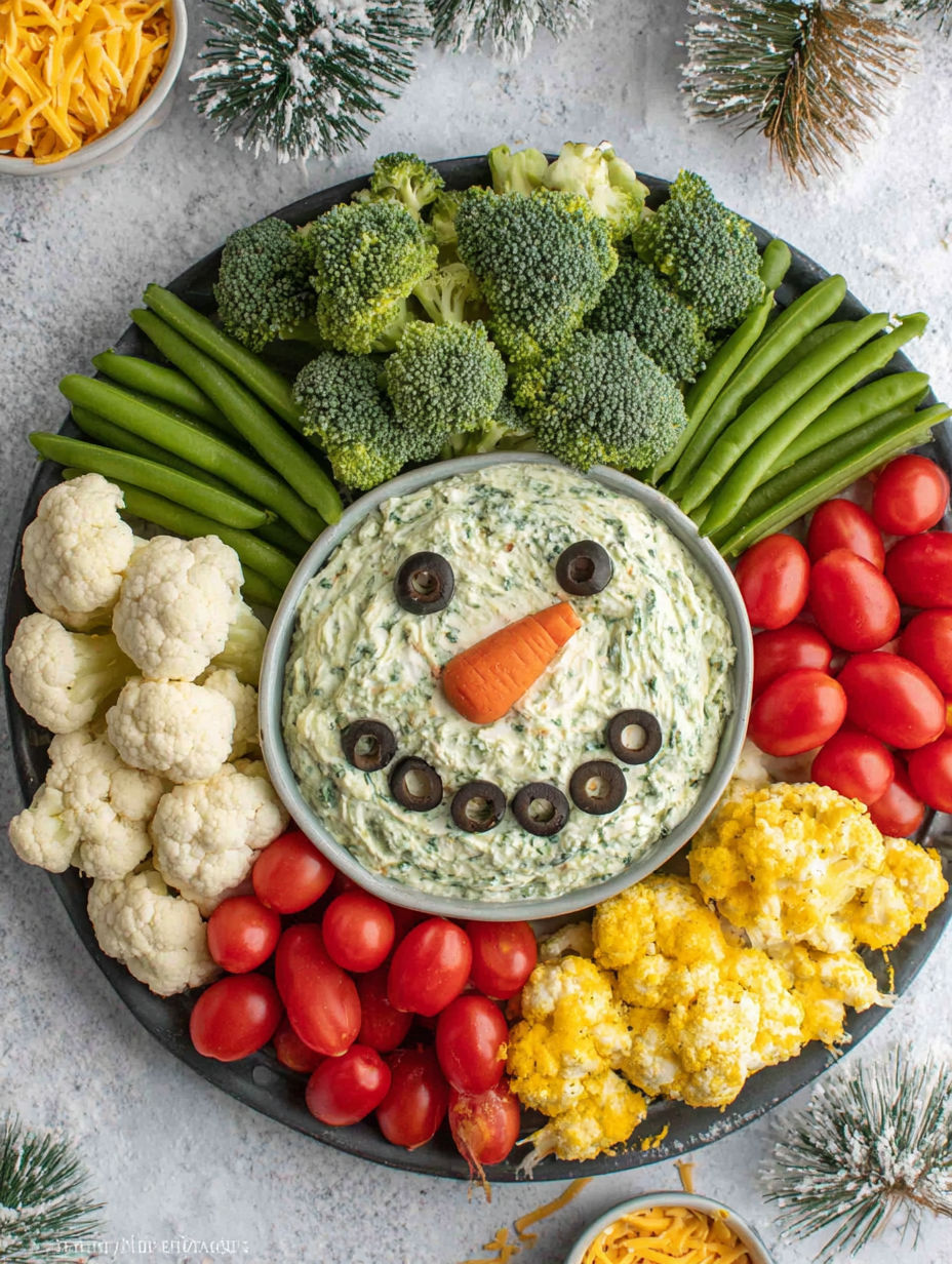 A veggie platter with a snowman made out of vegetables and two dips.