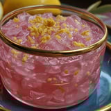 A bowl of pink gelatin with yellow fruit on top.