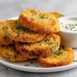 A plate of fried green tomatoes with a side of dipping sauce.