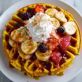 A plate of waffles with bananas, strawberries, and whipped cream.