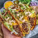 A person is holding a smash burger taco.