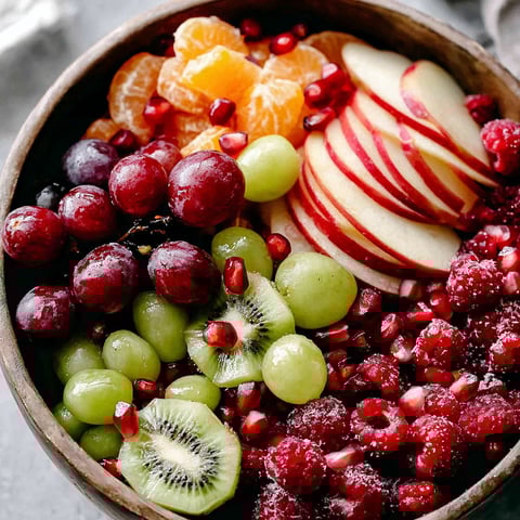 A bowl of fruit salad with kiwi, apples, oranges, grapes, and pomegranates.