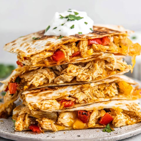 A stack of chicken quesadillas with white cheese and green toppings.