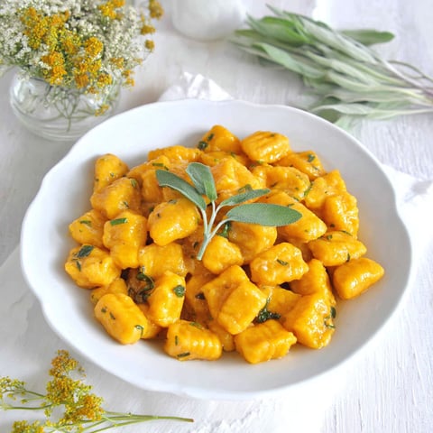 A bowl of gnocchi with a green herb on top.
