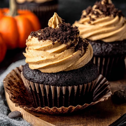 Two chocolate pumpkin cupcakes on a wooden tray.