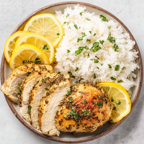 A plate of food with chicken, rice, and lemon.