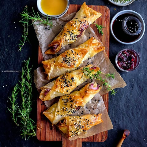 A wooden cutting board with a tray of cranberry and brie filo crackers.