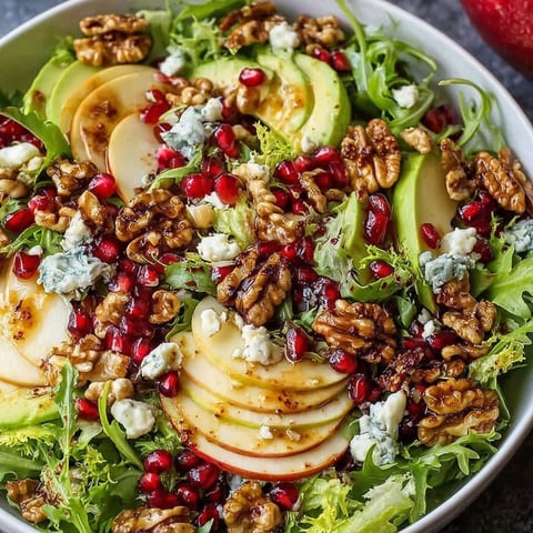A bowl of salad with pomegranate, walnuts, and blue cheese.