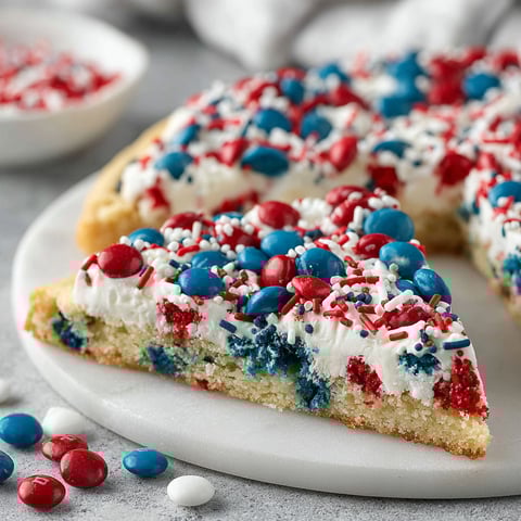 A slice of a sugar cookie cake with red, white and blue decorations.